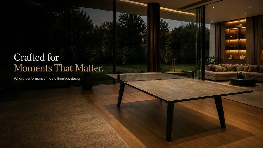 ARGMAC table tennis table with a stone-textured top and angled black legs, table tennis net in place, set in a warmly lit room facing a garden at dusk, sofa in the background.