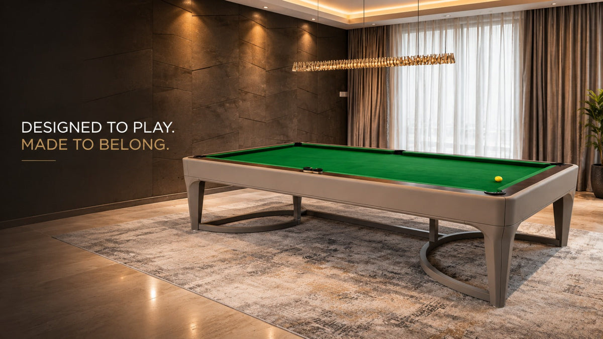 ARGMAC Negrosno billiards table in a taupe finish with curved, oval metal legs and green cloth, set in a warm luxury lounge with textured stone walls and a gold pendant chandelier.
