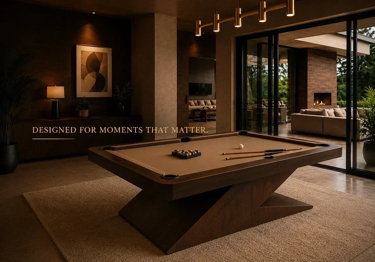  ARGMAC pool table in dark wood with a Z-shaped base and tan pool cloth, racked pool balls and a billiard pool cue on top, set in a warm lounge with a fireplace beyond. 